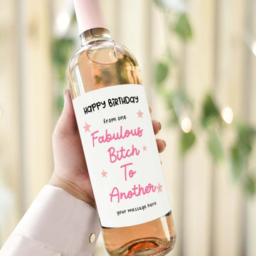 A wine bottle with a birthday label reading "Happy Birthday from one fabulous bitch to another" in pink and black text with star accents.