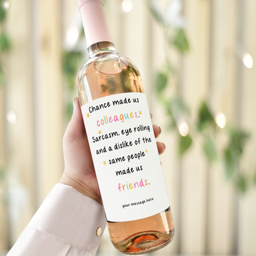 Personalised wine label reading "Chance made us colleagues, sarcasm and shared dislikes made us friends" on a wine bottle held in hand.
