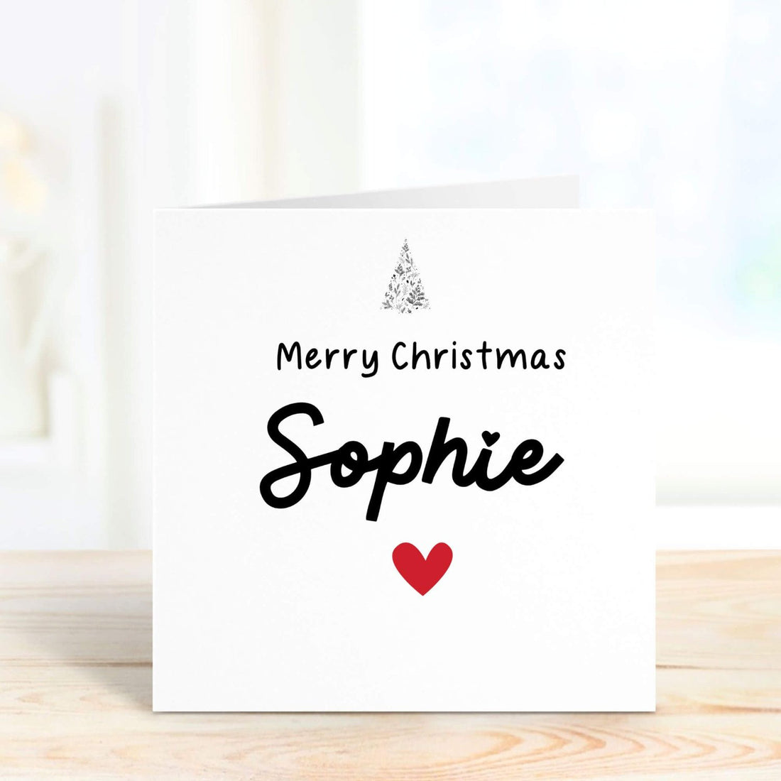 Personalised Christmas card with "Merry Christmas [Name]" message, featuring a festive tree and red heart. Perfect for sending holiday wishes with a custom name.