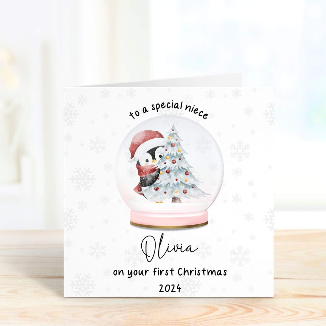 Personalised first Christmas card for niece featuring a snow globe with a penguin and Christmas tree, customised with her name and the year 2024.
