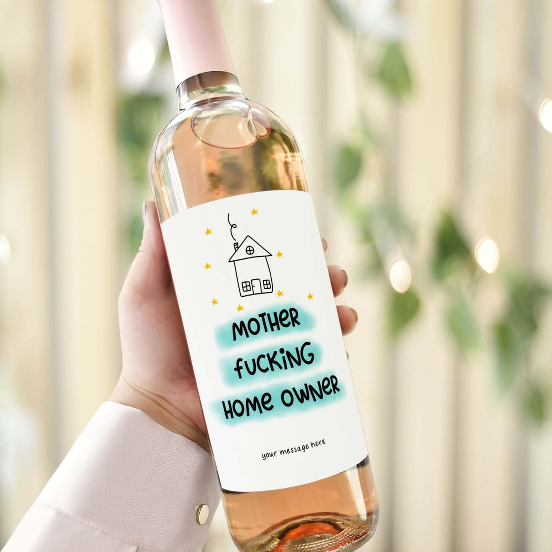 A wine bottle with a funny housewarming label reading "Mother F***ing Home Owner," designed as a gift for celebrating new homeowners.